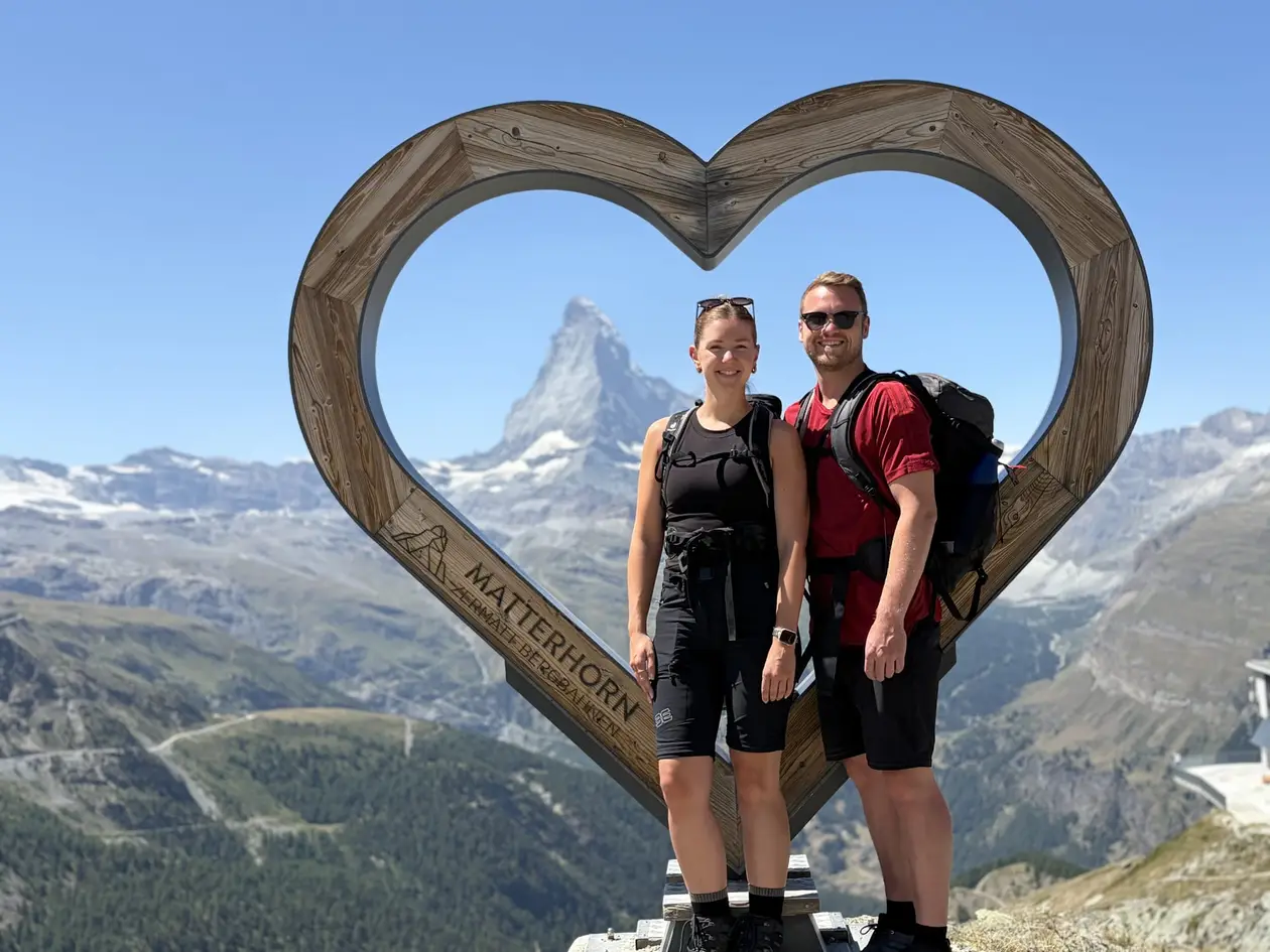 Max und Rebecca stehen in einem großen Holzrahmen in Herzform mit der Aufschrift Matterhorn, durch den Rahmen sieht man das Matterhorn