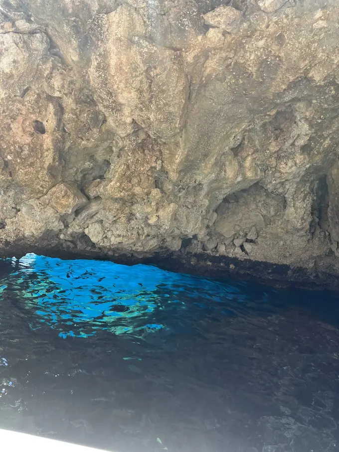 Überhängende Felswand, darunter leuchtend blaues Wasser am Eingang einer Höhle