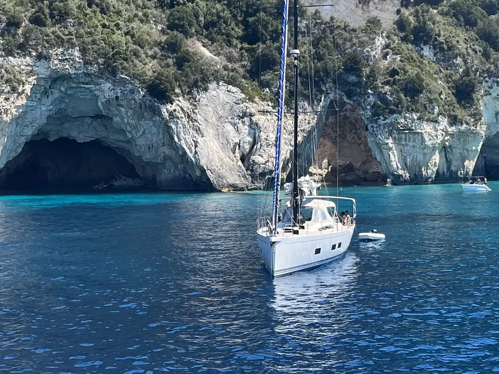 Eine Segelyacht ankert vor einer Felsküste mit großen Höhlenöffnungen über blauem Wasser