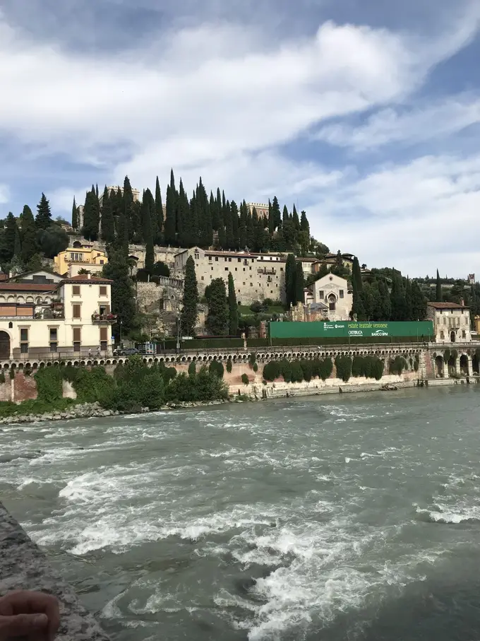 Der Hügel mit Zypressen und dem Castel San Pietro, vom anderen Ufer der schnell fließenden Etsch aus gesehen