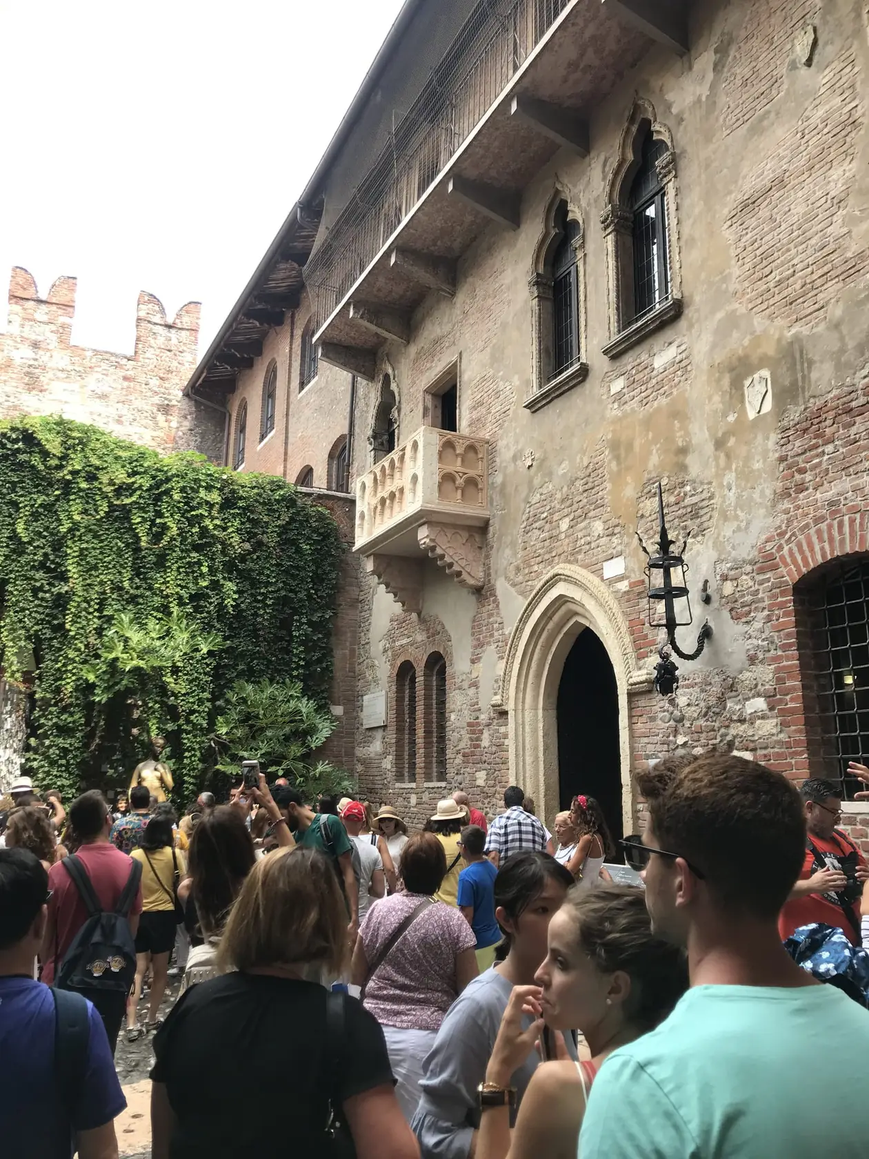Innenhof mit efeubewachsener Mauer und dem steinernen Balkon an einer alten Backsteinfassade, darunter dicht gedrängte Besucher