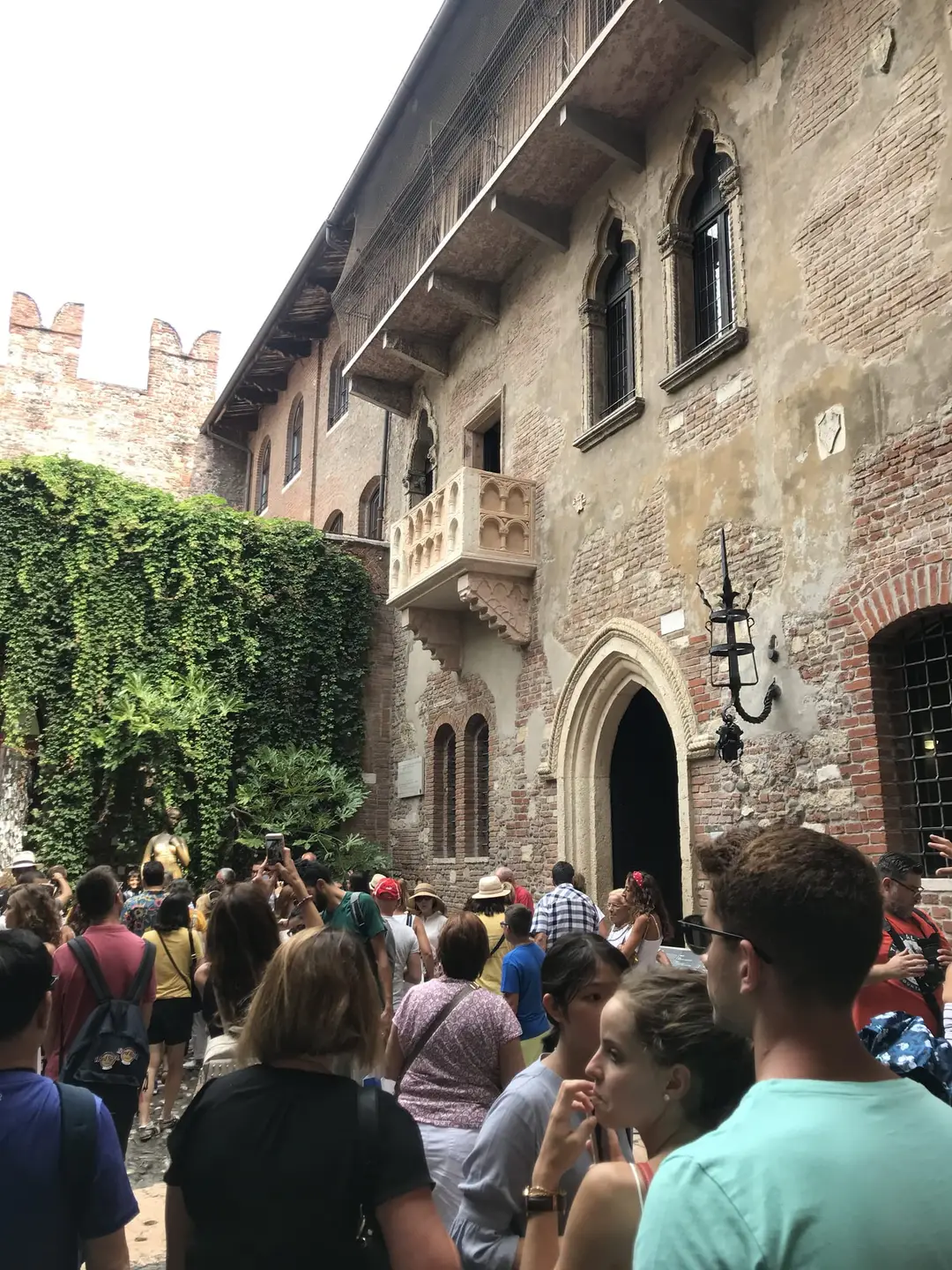 Innenhof mit efeubewachsener Mauer und dem steinernen Balkon an einer alten Backsteinfassade, darunter dicht gedrängte Besucher