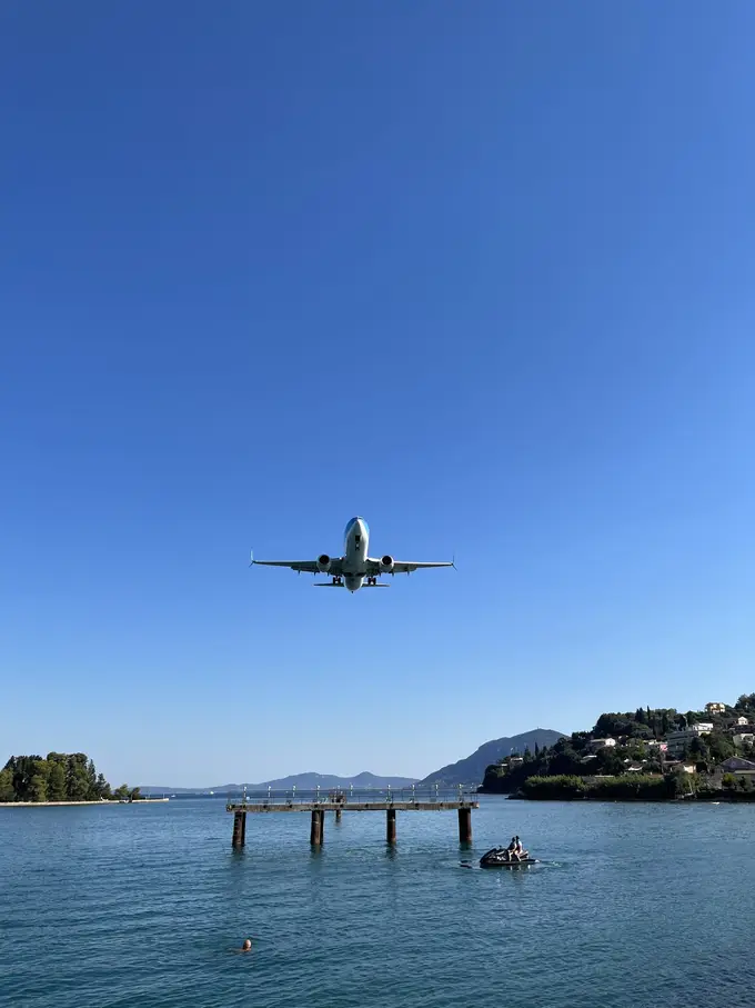 Ein Passagierjet im Anflug über dem Wasser, darunter ein Steg und ein kleines Boot