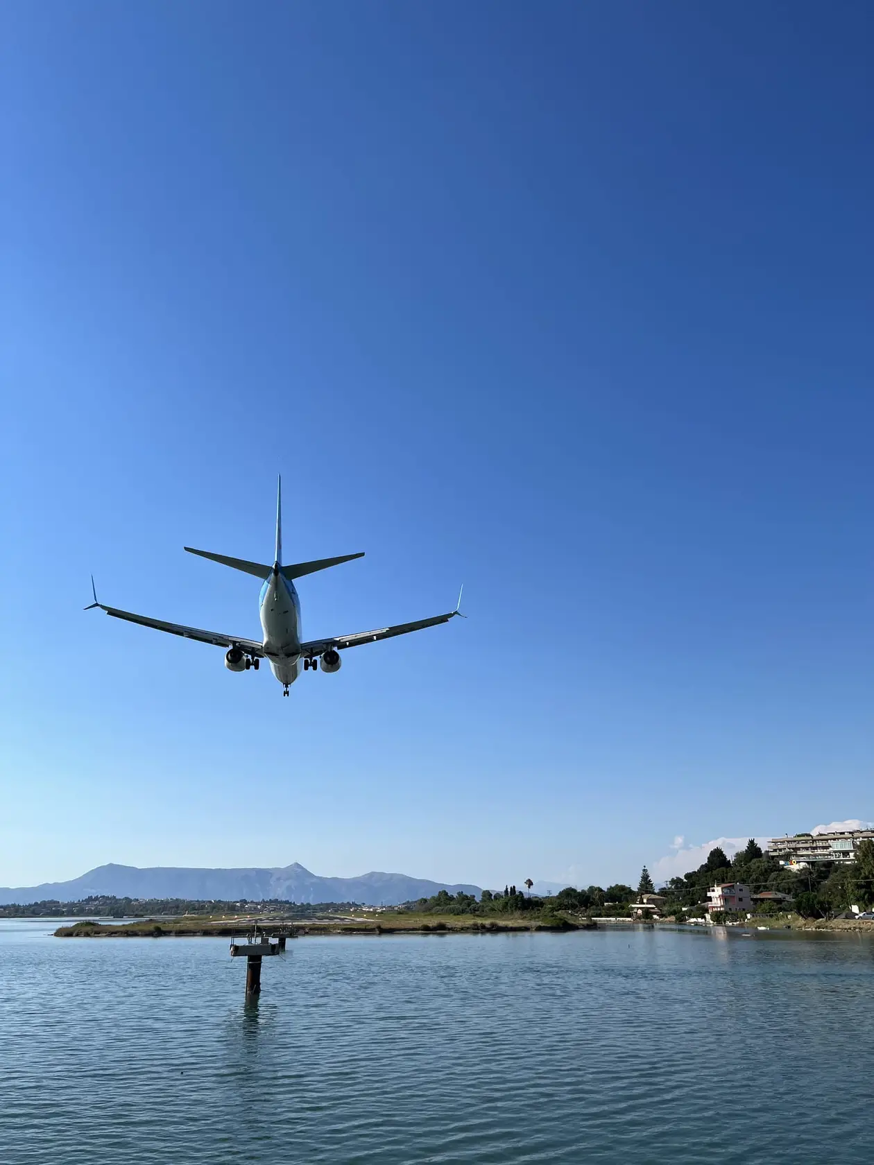 Ein Passagierjet fliegt tief über die Lagune, unten ein Steg im Wasser