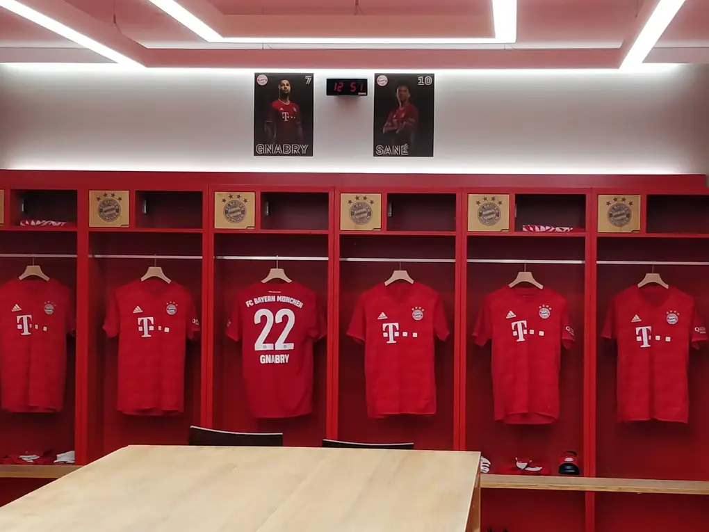 Die Kabine mit roten Spinden, in jedem hängt ein rotes Trikot, in der Mitte die Nummer 22 von Gnabry, darüber Spielerporträts
