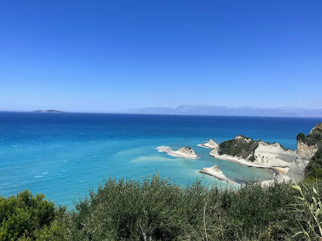 Weiße Felsnadeln und kleine Felsinseln am Ende einer Landzunge, ringsum türkises Meer