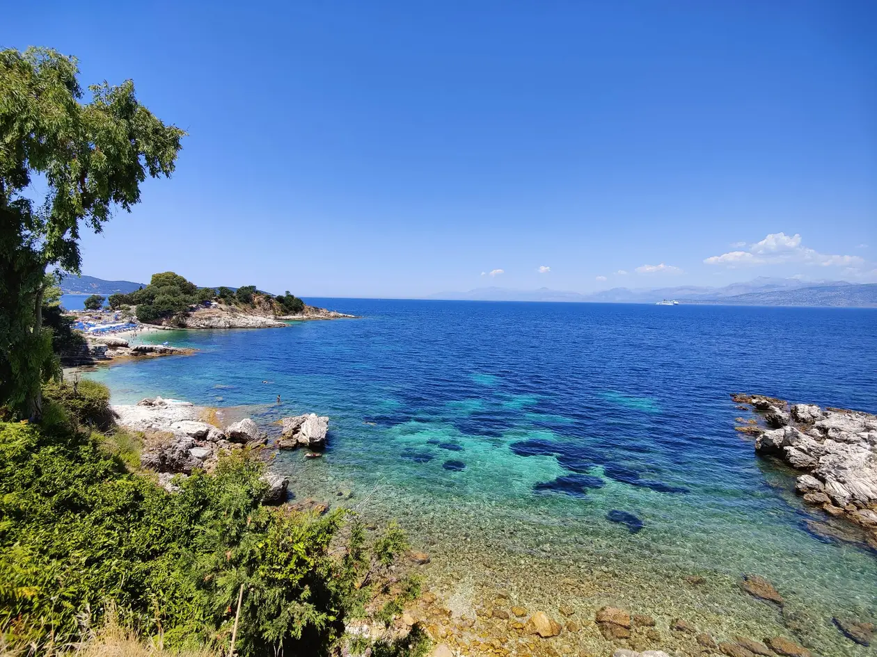 Klares, türkises Wasser über Steinen zwischen hellen Felsen, dahinter eine kleine Landzunge und das Festland