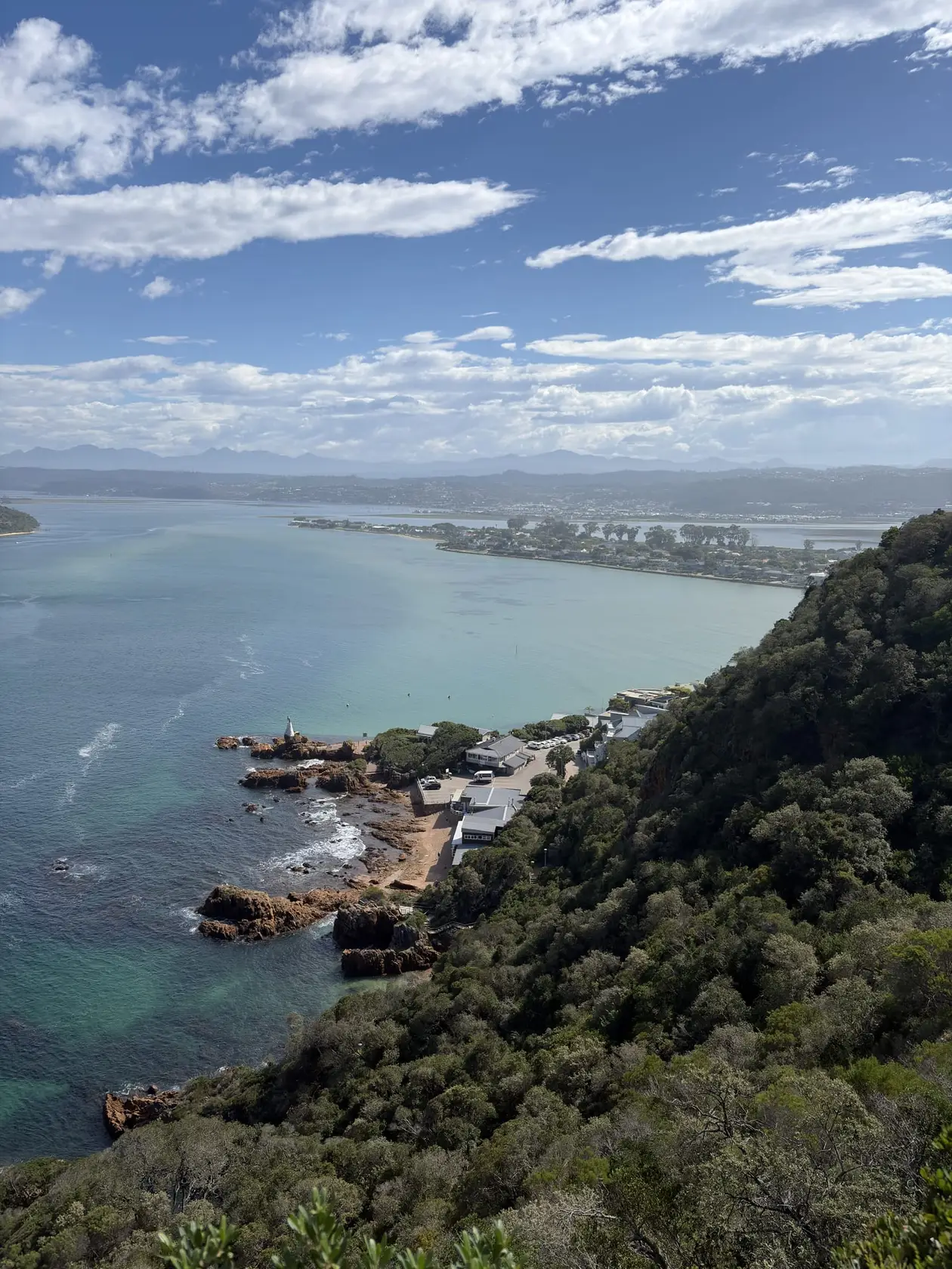 Blick von oben auf die schmale Einfahrt zwischen den beiden bewaldeten Felsköpfen der Knysna Heads