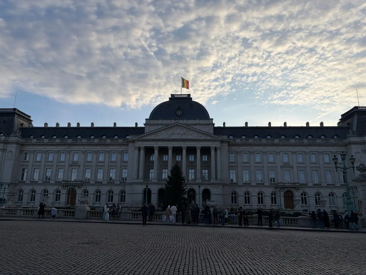 Die lange Fassade des Königspalasts mit Säulenportal und Kuppel, oben die belgische Flagge, davor ein gepflasterter Platz mit Besuchern