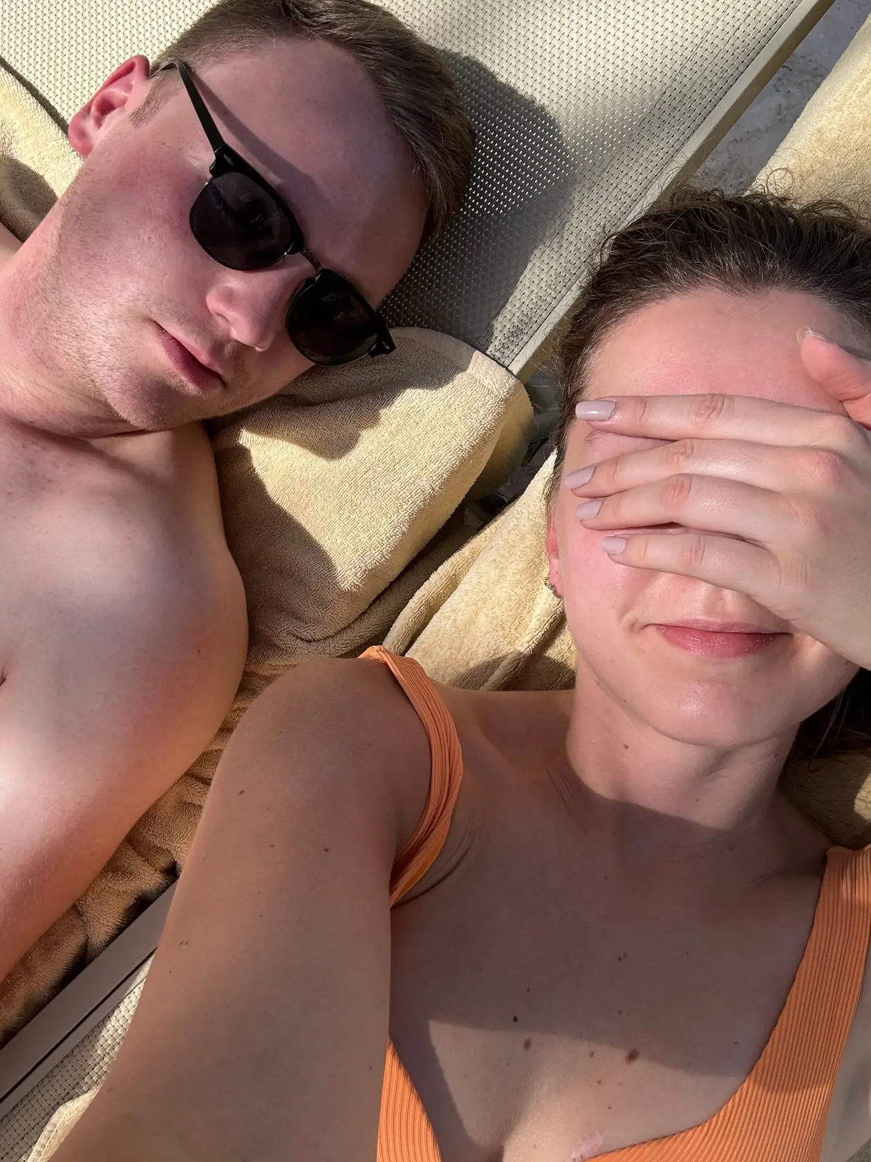 Selfie von Max und Rebecca auf zwei Liegen mit Handtüchern, Max mit Sonnenbrille, Rebecca hält sich eine Hand vor die Augen