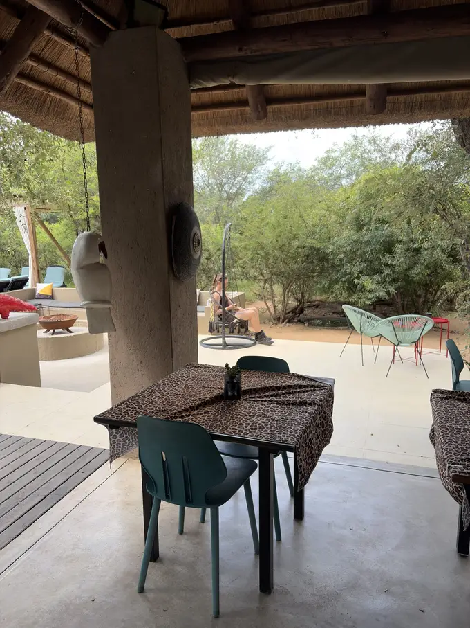 Überdachter Lounge-Bereich der Lodge mit Tischen, Sitzkissen und Blick ins Grüne