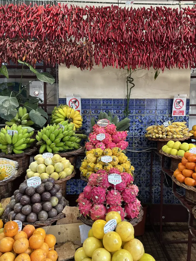 Marktstand mit aufgehängten roten Chilischoten, Bananen, Drachenfrüchten und Zitrusfrüchten