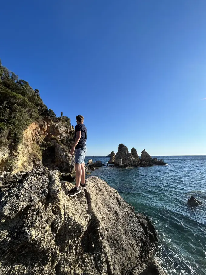 Max steht auf einem Felsen am Meer, im Wasser dahinter eine Gruppe spitzer Felsinseln