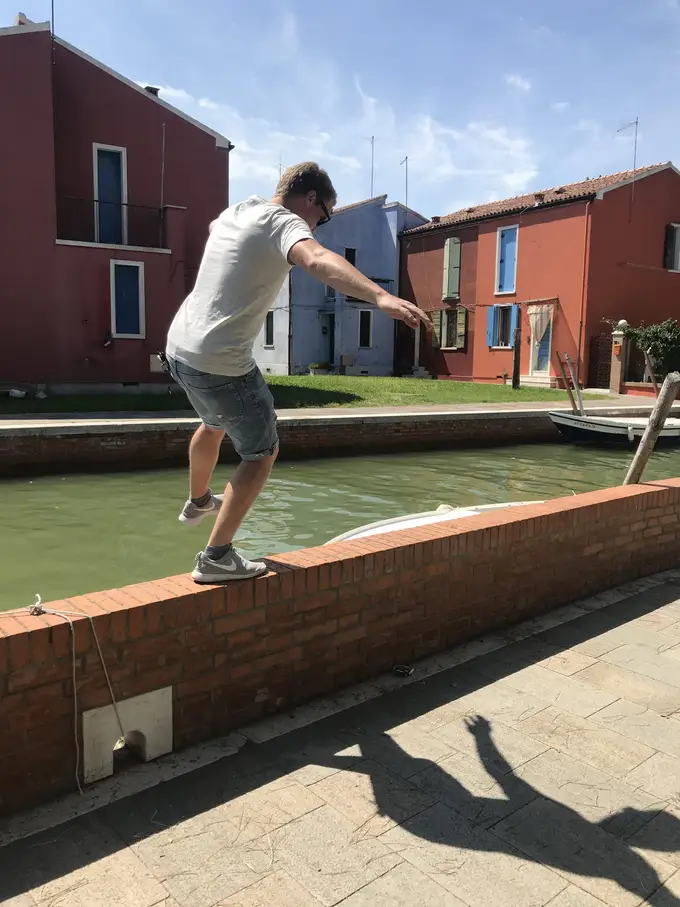 Max balanciert mit ausgebreiteten Armen auf einer niedrigen Backsteinmauer am Kanal, vor roten Häusern