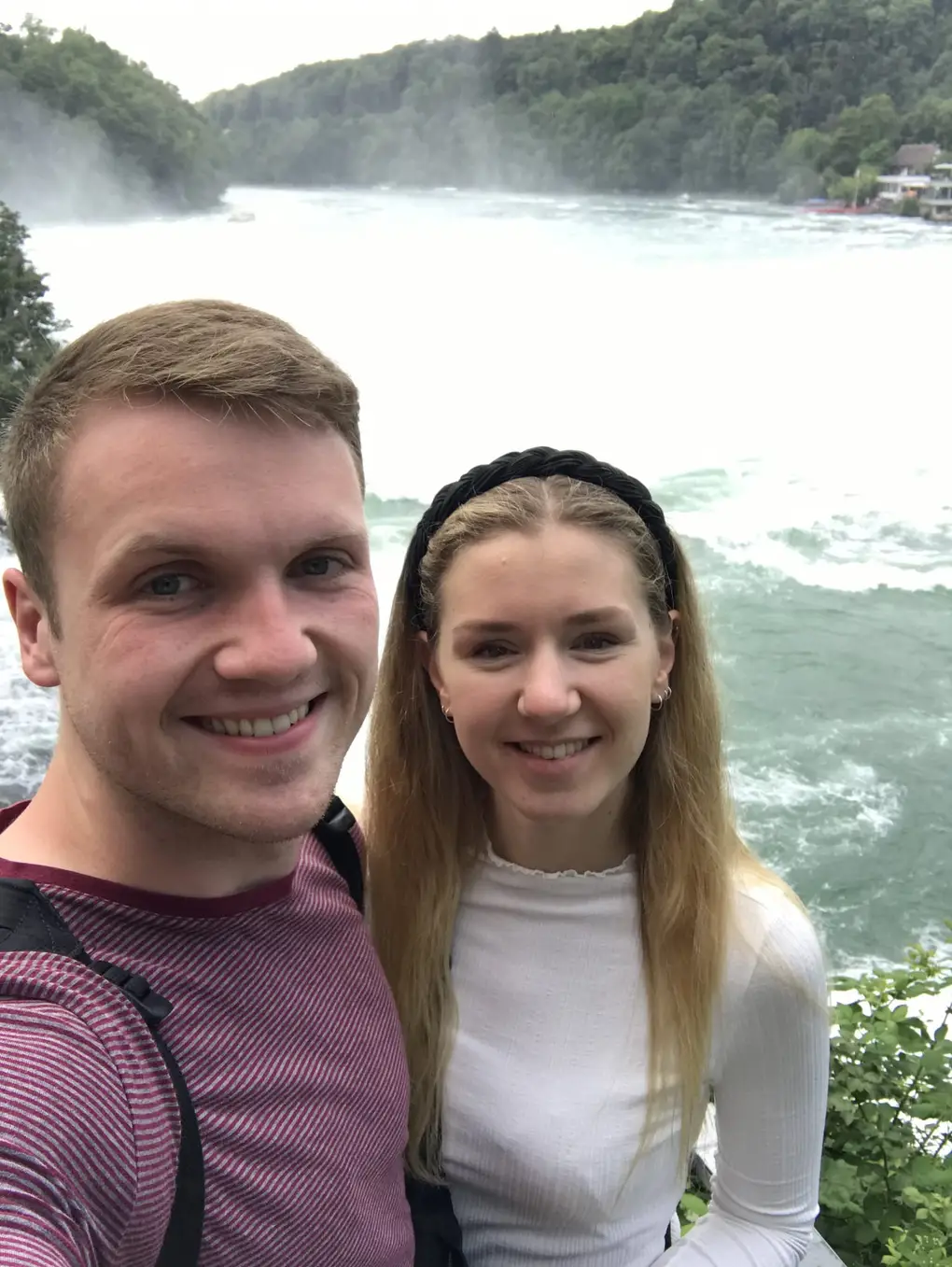 Selfie von Max und Rebecca, hinter ihnen das aufgewühlte grüne Wasser unterhalb des Falls und bewaldete Hänge