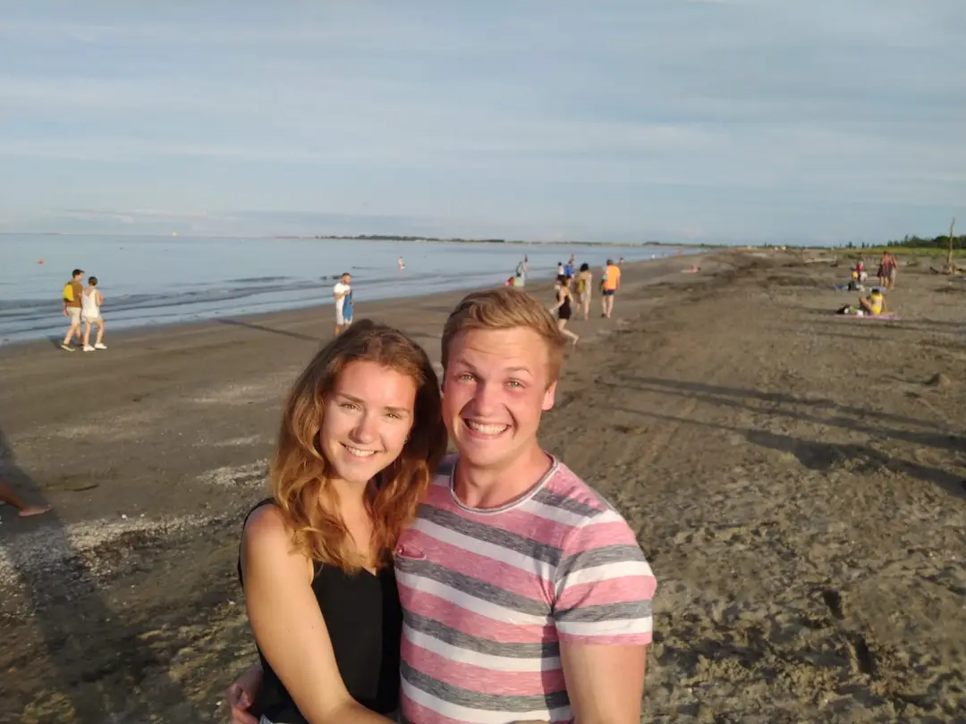 Rebecca und Max am breiten Sandstrand im Abendlicht, dahinter Spaziergänger am Wasser
