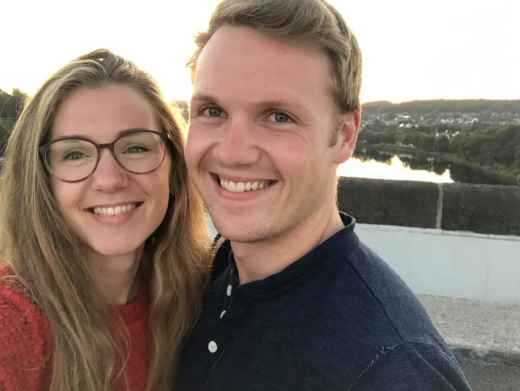 Selfie von Rebecca mit Brille und Max auf der Staumauer, hinter ihnen die Brüstung und ein Gewässer im Tal in der Abendsonne