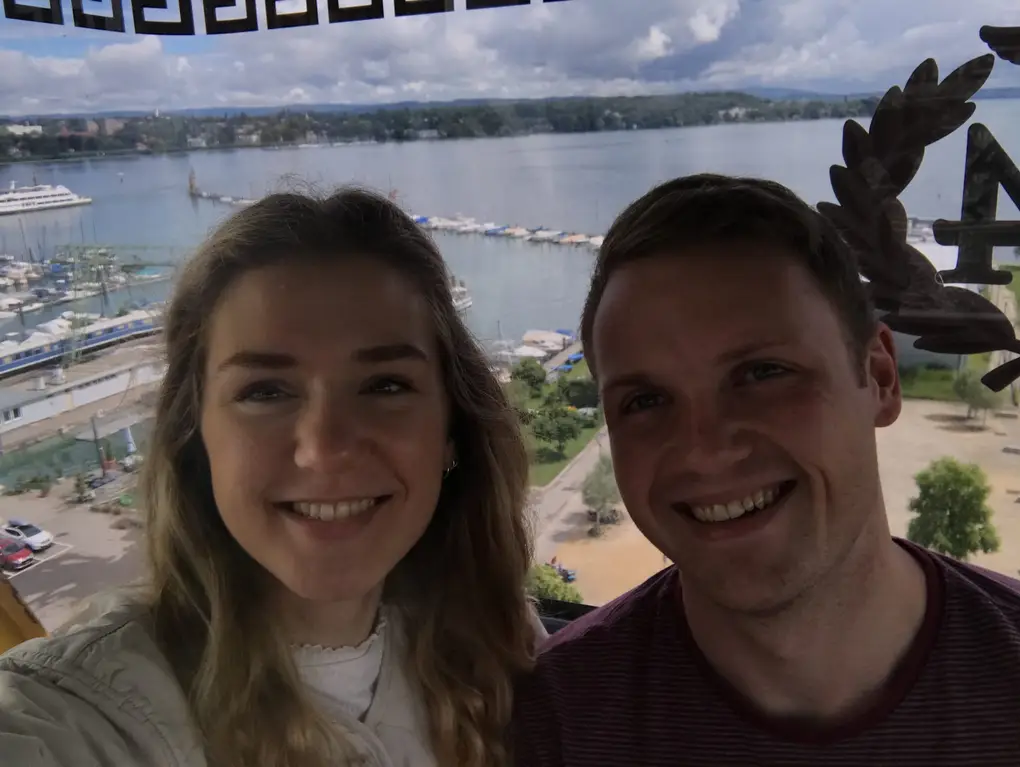 Selfie von Rebecca und Max in einer Gondel des Riesenrads, hinter der Scheibe der Hafen mit Booten, ein Ausflugsschiff und der See