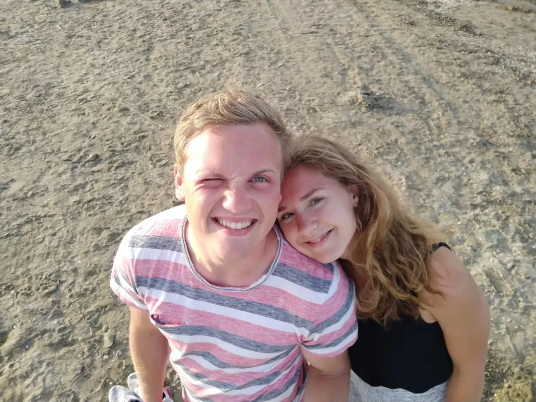 Max und Rebecca sitzen lachend im Sand, Kopf an Kopf