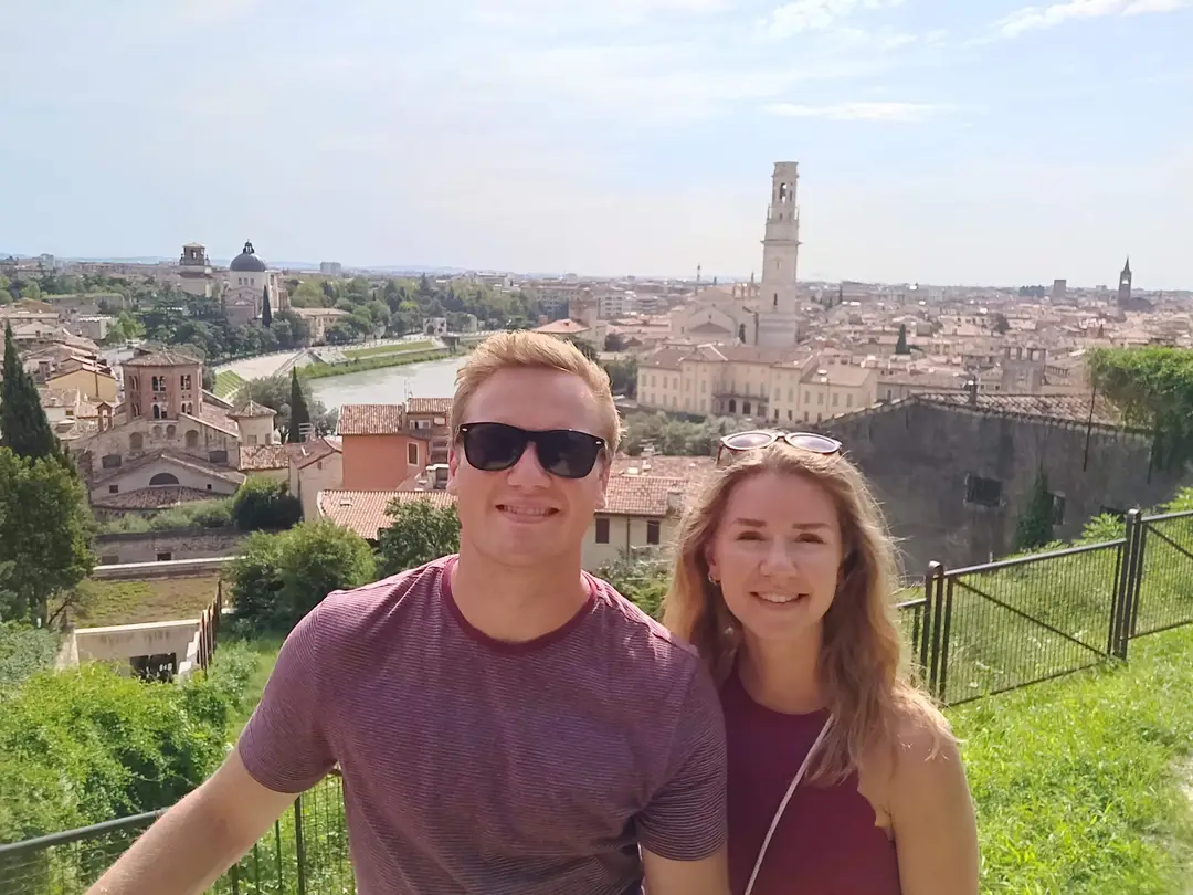 Max und Rebecca an einem Geländer hoch über Verona, hinter ihnen die Dächer der Altstadt und ein hoher Glockenturm