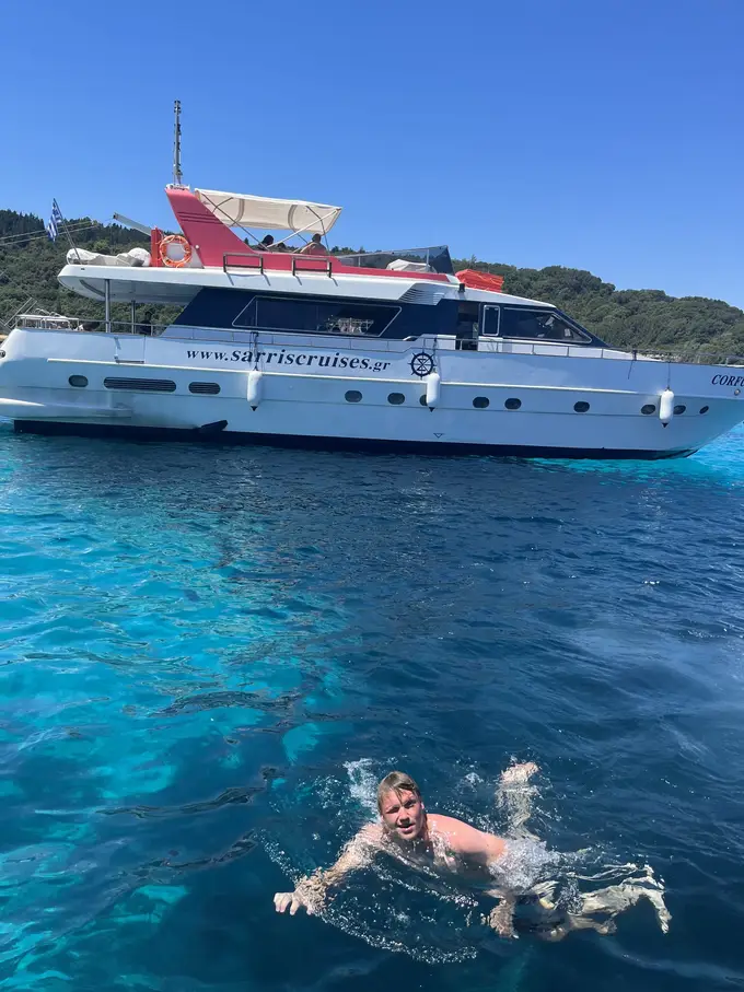Max schwimmt in klarem türkisem Wasser, hinter ihm eine große weiße Motoryacht