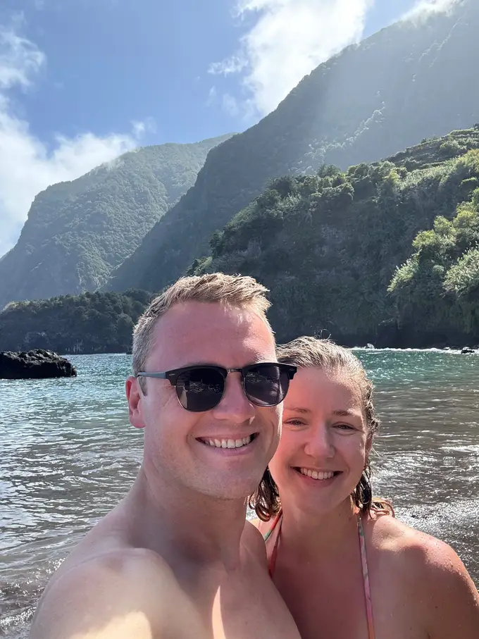 Max und Rebecca lächeln in die Kamera, dahinter das Meer und steile grüne Klippen