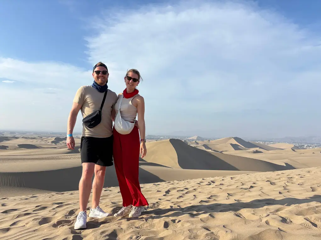 Max und Rebecca stehen auf einem Dünenkamm, hinter ihnen ein Meer aus Sanddünen und eine große Wolke