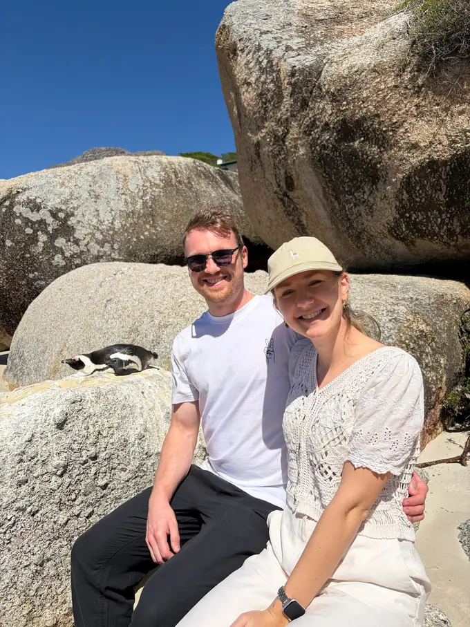 Max und Rebecca sitzen zusammen auf einem Felsen, ein Pinguin schaut aus einer Felsspalte