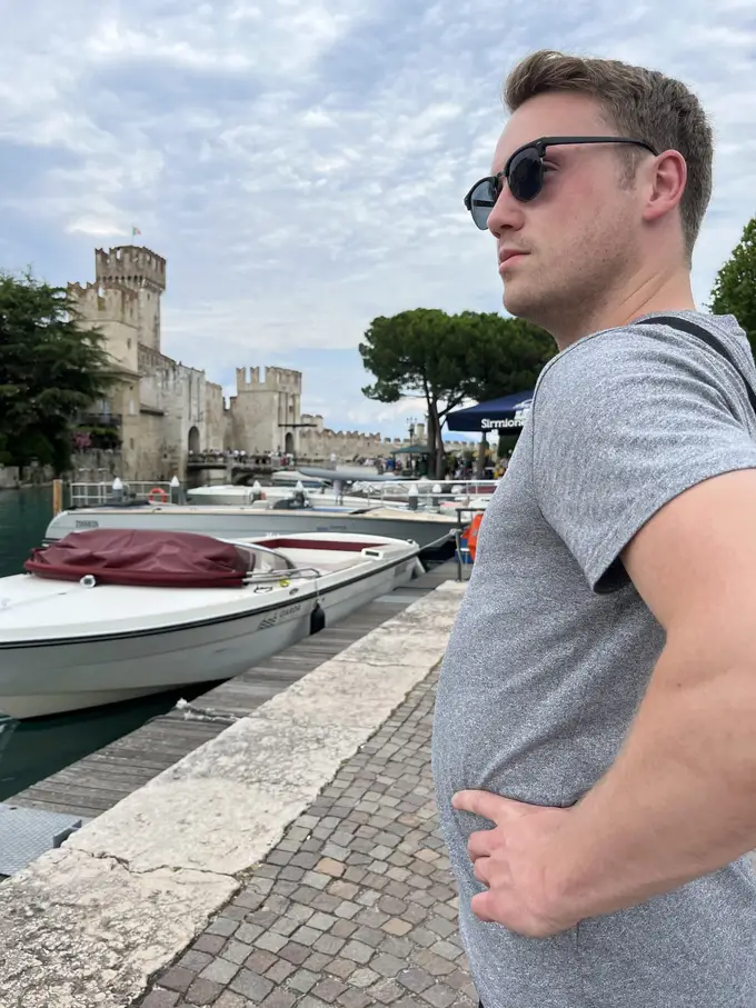 Max mit Sonnenbrille im Profil an einem Bootssteg, im Hintergrund Motorboote und die Türme der Scaligerburg
