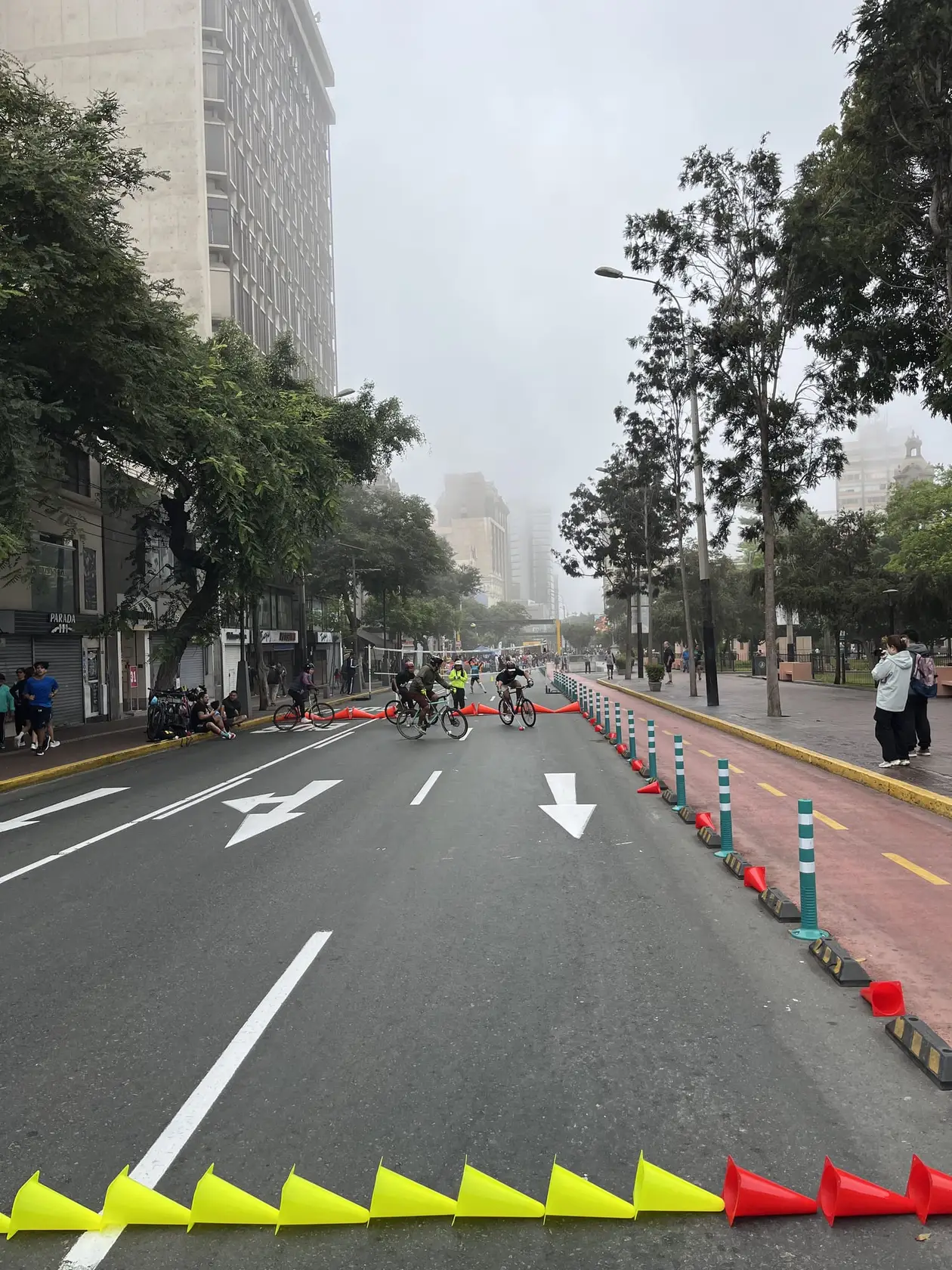 Breite, für Autos gesperrte Straße in Miraflores mit Hütchen und Radfahrern, die Hochhäuser verschwinden im grauen Hochnebel