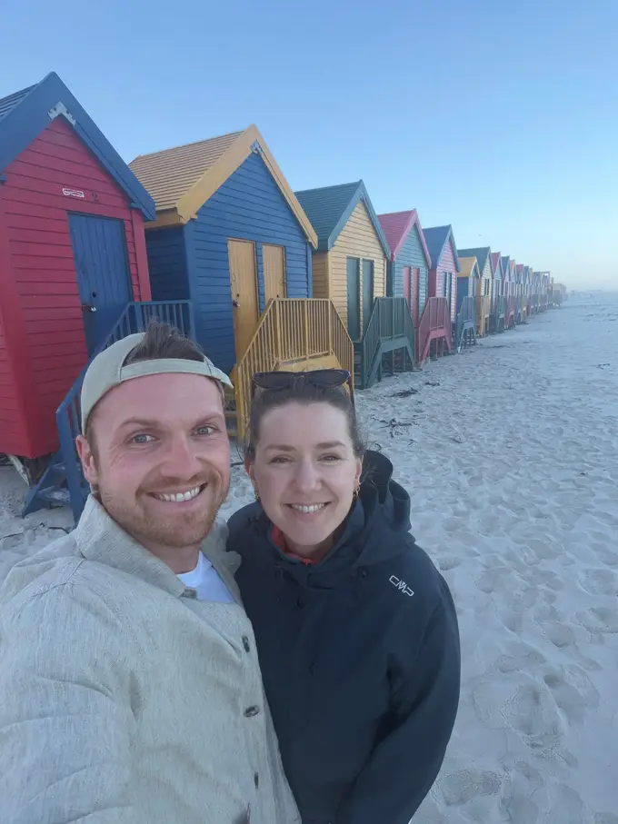Max und Rebecca vor den bunten Strandhäuschen von Muizenberg in der Abenddämmerung