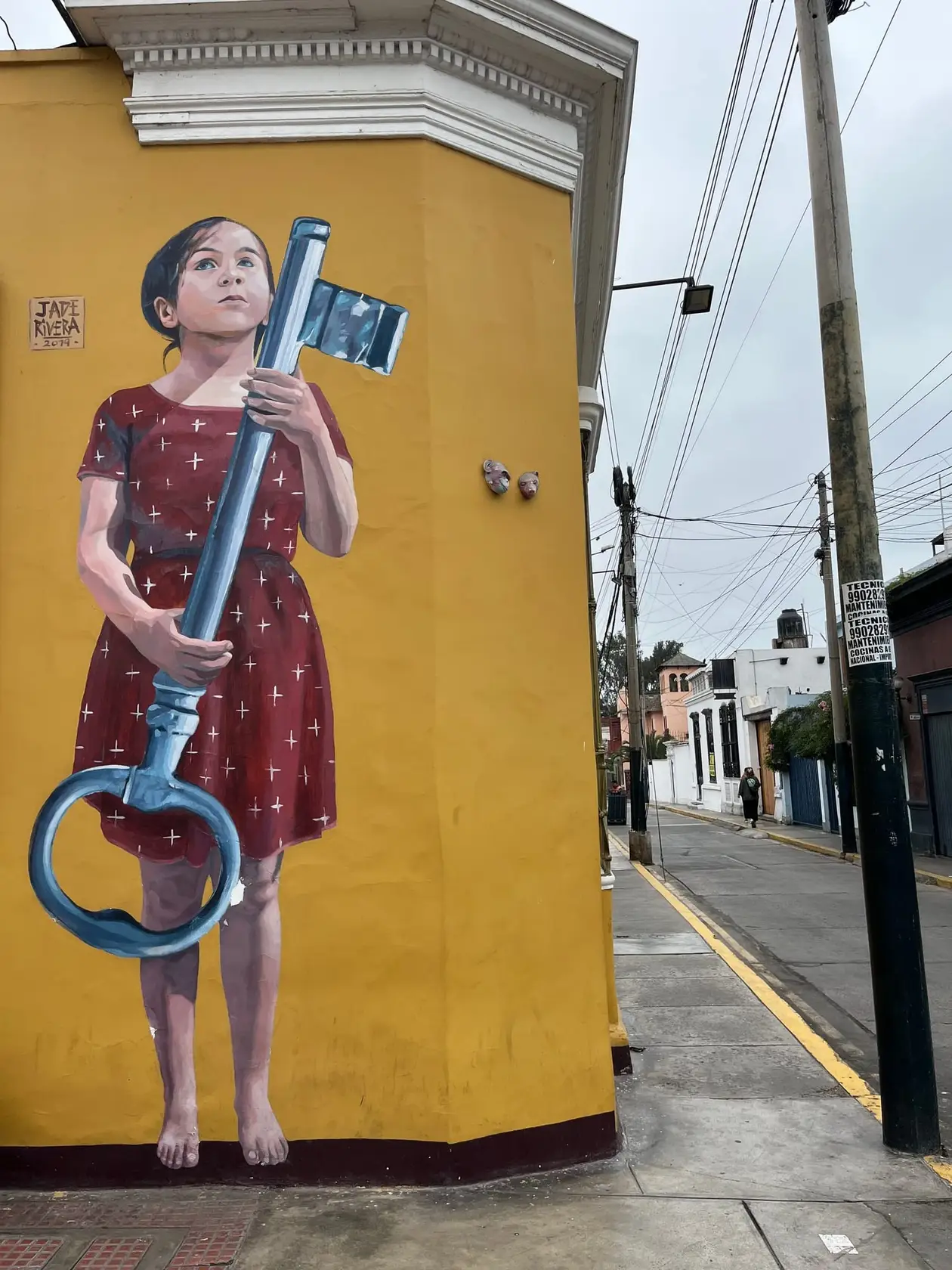 Wandbild eines Mädchens im roten Kleid, das einen überdimensionalen Schlüssel hält, auf einer gelben Hauswand in Barranco