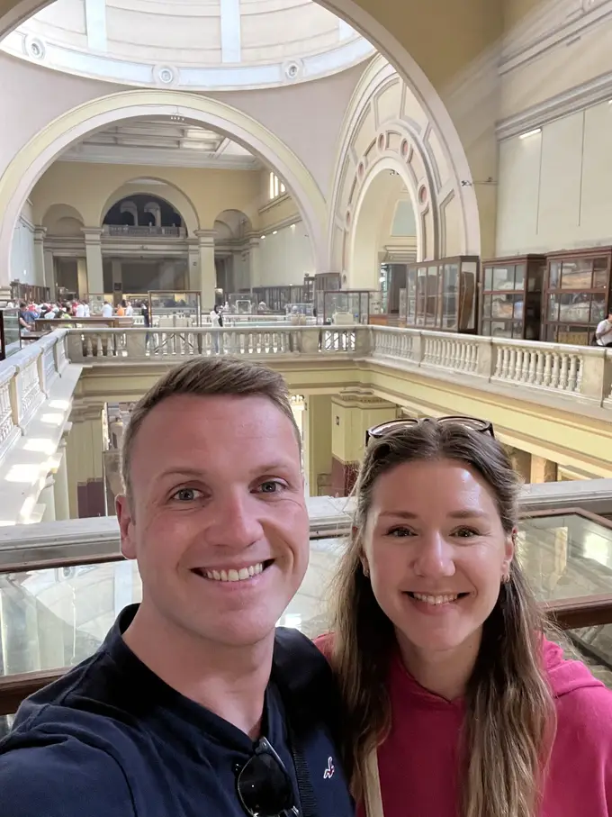 Selfie von Max und Rebecca auf der Galerie des Museums, hinter ihnen Rundbögen, Vitrinen und Besucher