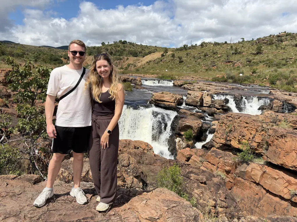 Max und Rebecca stehen vor einem kleinen Wasserfall in felsigem Gelände