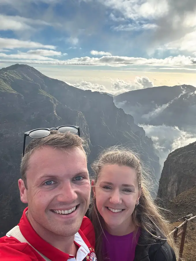 Max und Rebecca lächeln in die Kamera, im Tal darunter bildet sich das Wolkenmeer im Abendlicht