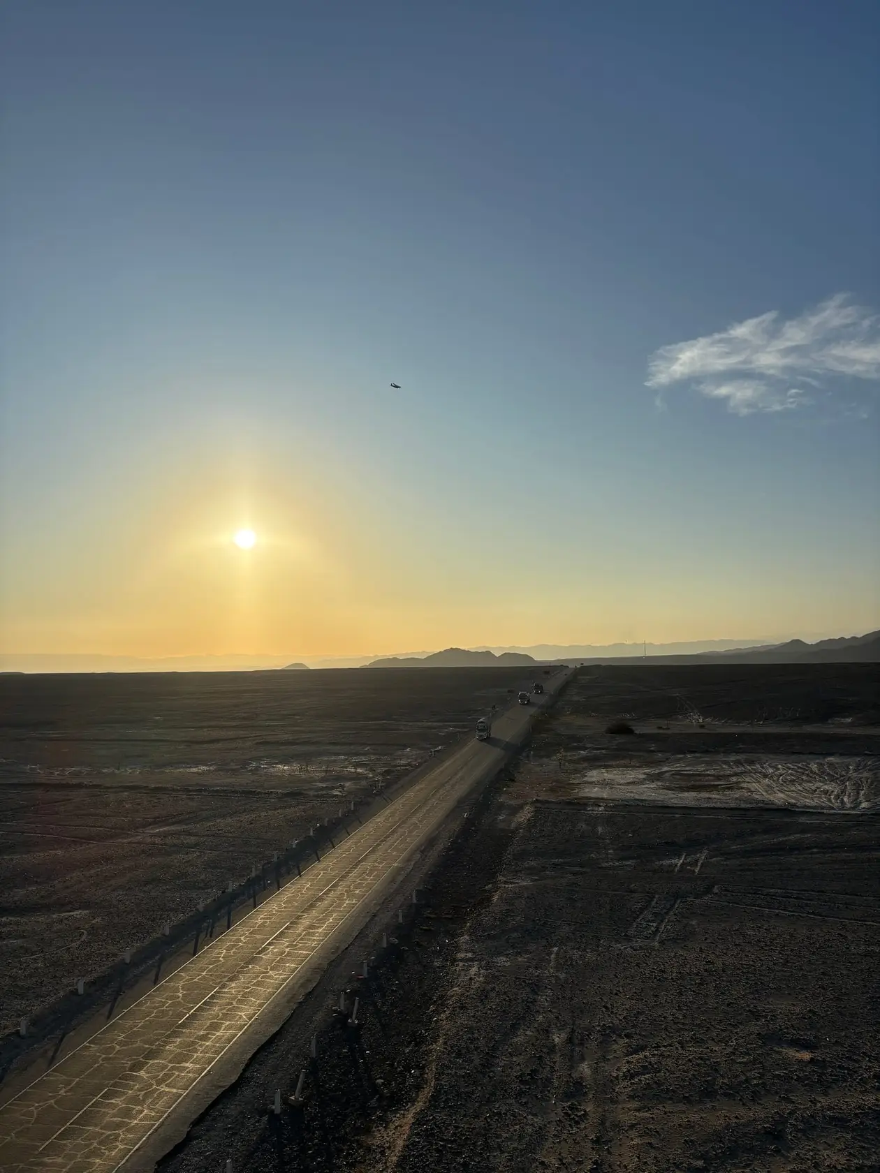 Die Panamericana läuft schnurgerade durch die dunkle Wüste, darüber steht die Sonne schon tief