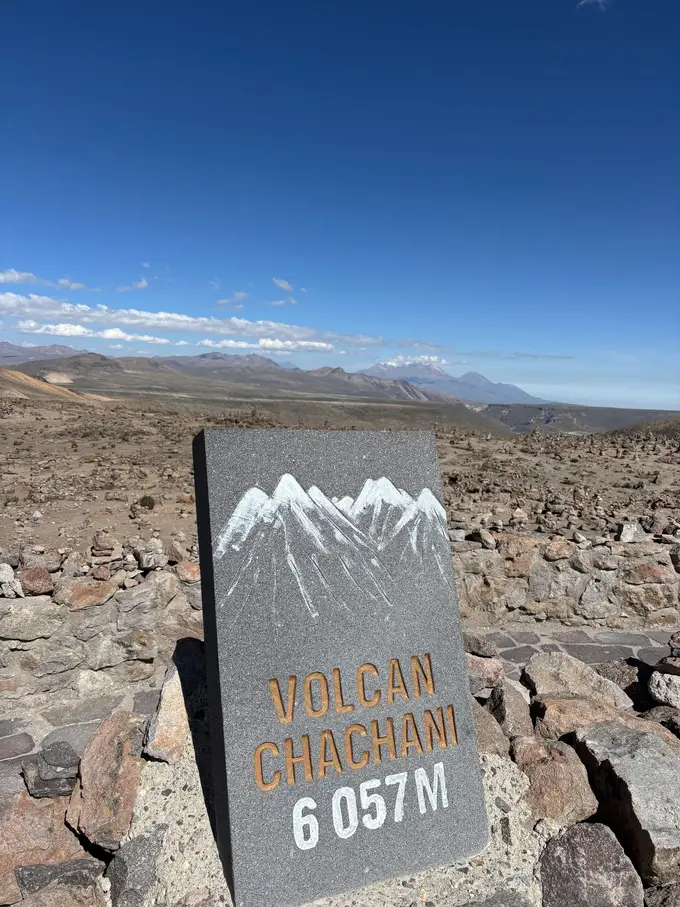 Steintafel mit der Aufschrift Volcán Chachani 6057 m in einer Hochebene voller aufgeschichteter Steinmännchen