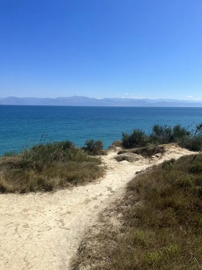 Sandiger Pfad durch trockenes Gras und Büsche oberhalb des Meeres