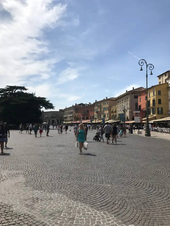 Die weite gepflasterte Piazza Bra mit Passanten, am Rand eine Häuserzeile und eine Straßenlaterne