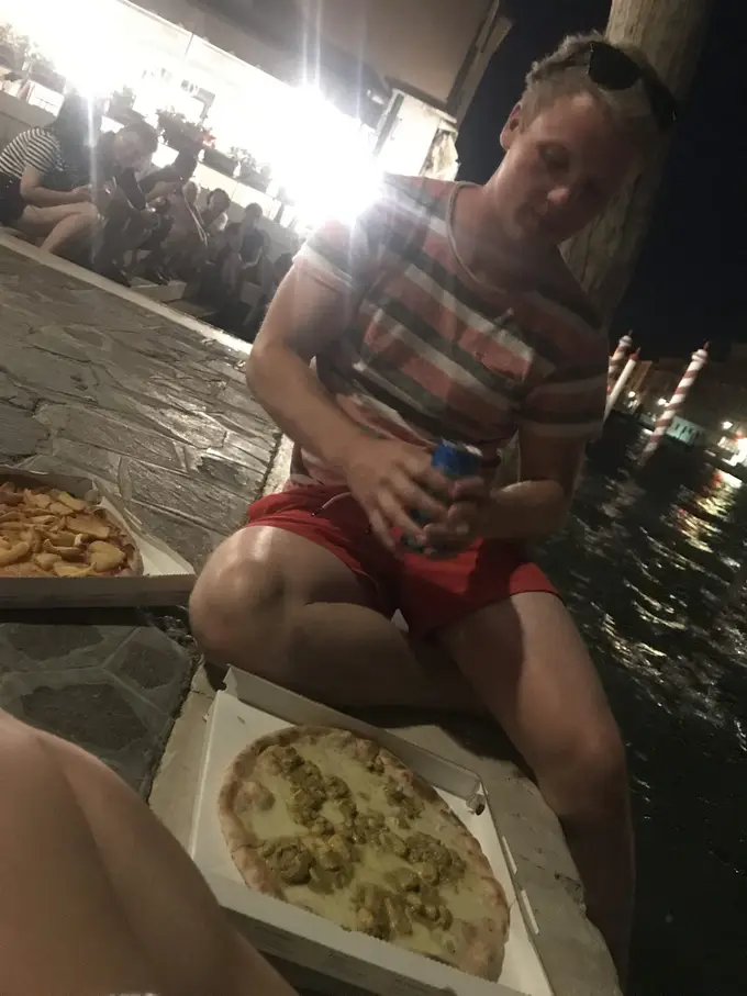 Max sitzt abends am Wasser vor einem geöffneten Pizzakarton