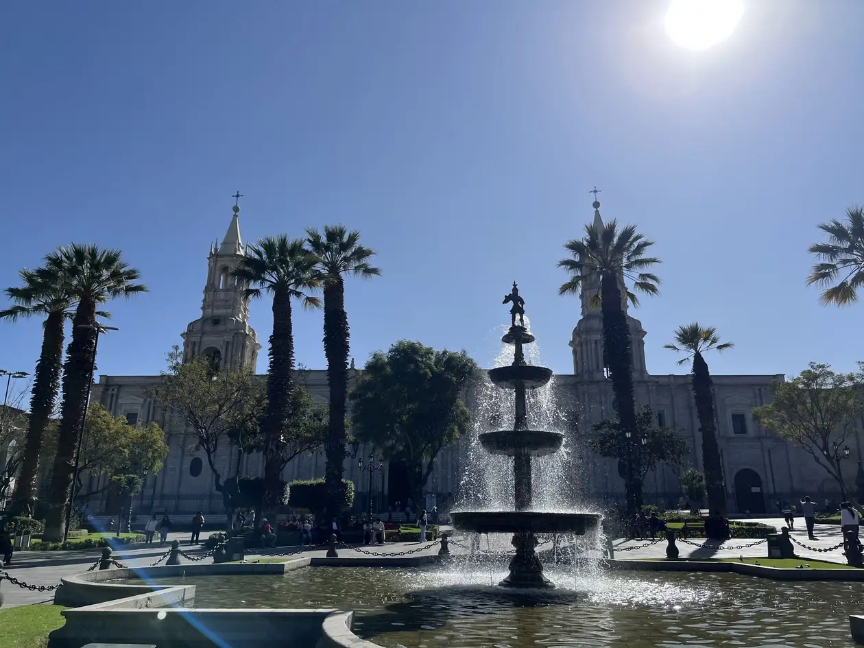 Brunnen auf der Plaza de Armas von Arequipa zwischen Palmen, dahinter die weiße Kathedrale unter blauem Himmel