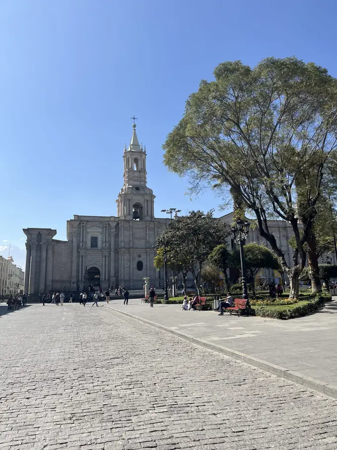 Weite gepflasterte Plaza de Armas mit Bäumen, hinten die Kathedrale mit ihrem Glockenturm