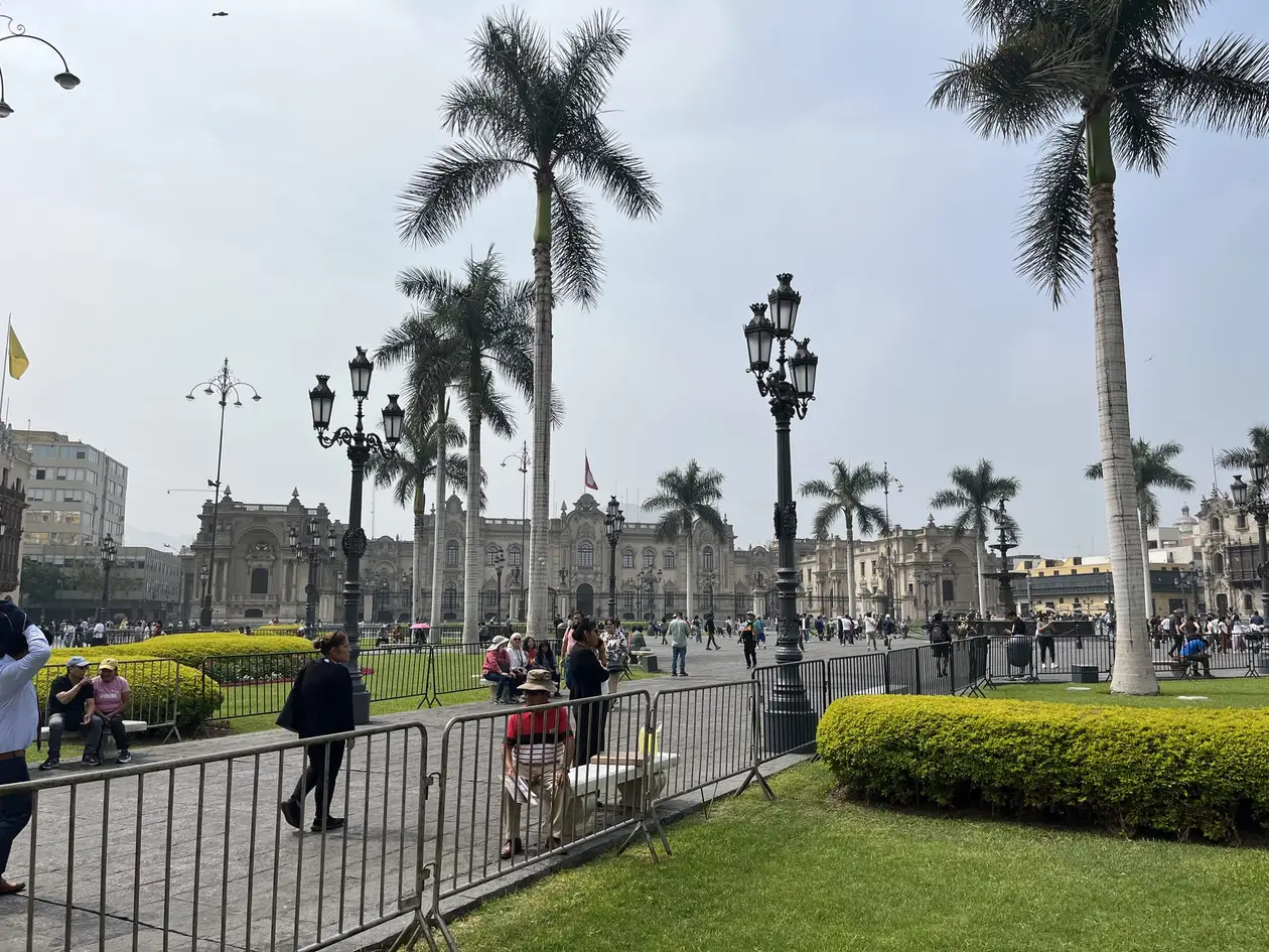 Plaza de Armas in Lima mit Königspalmen, schmiedeeisernen Laternen und gestutzten Hecken, dahinter der Regierungspalast