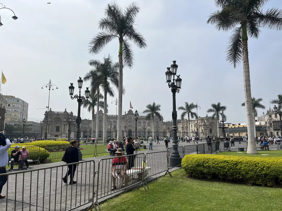 Plaza de Armas in Lima mit Königspalmen, schmiedeeisernen Laternen und gestutzten Hecken, dahinter der Regierungspalast