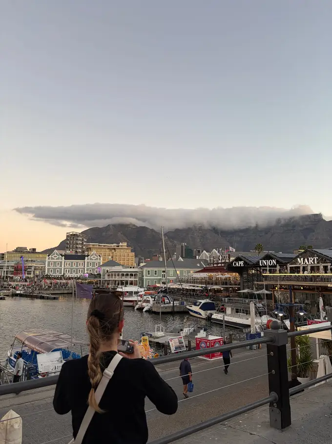 Eine Frau geht die Promenade der V&A Waterfront entlang, im Hintergrund der Tafelberg unter einer Wolkendecke