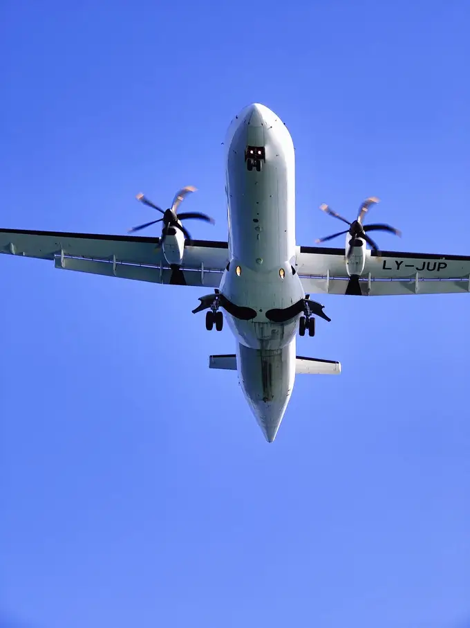 Eine Propellermaschine direkt über der Kamera, Fahrwerk ausgefahren, vor blauem Himmel