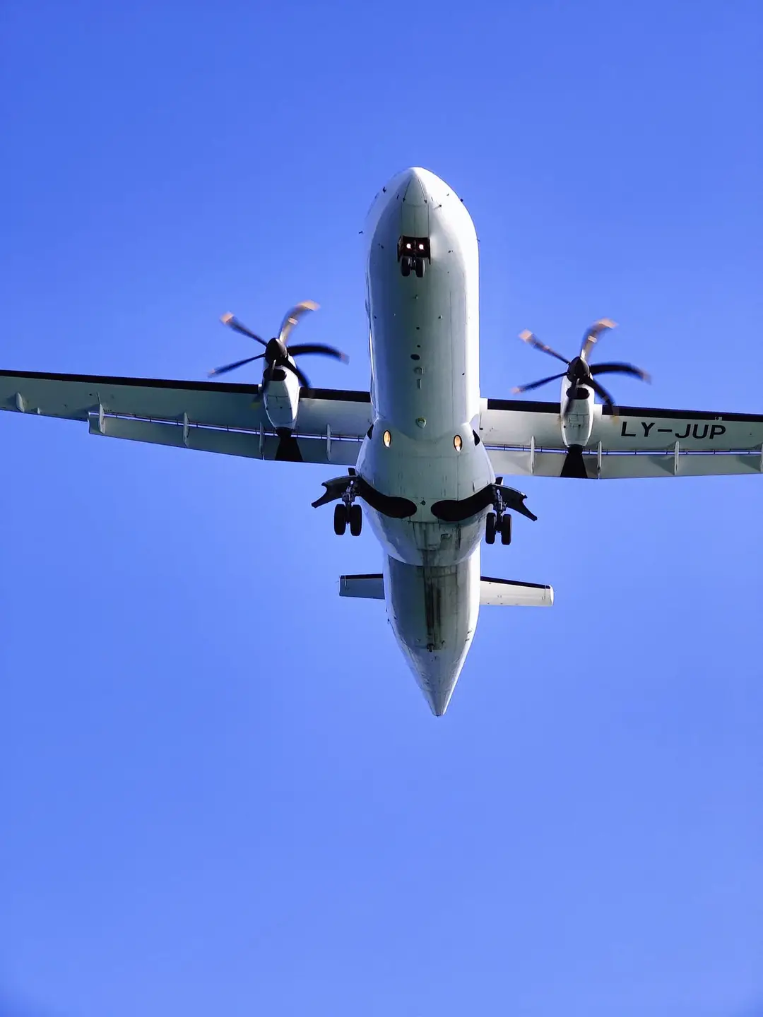 Eine Propellermaschine direkt über der Kamera, Fahrwerk ausgefahren, vor blauem Himmel