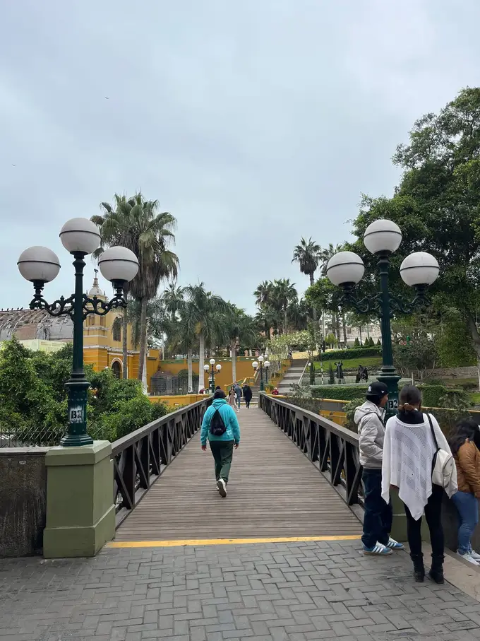 Die hölzerne Puente de los Suspiros mit weißen Laternen und Palmen, Menschen überqueren die Brücke