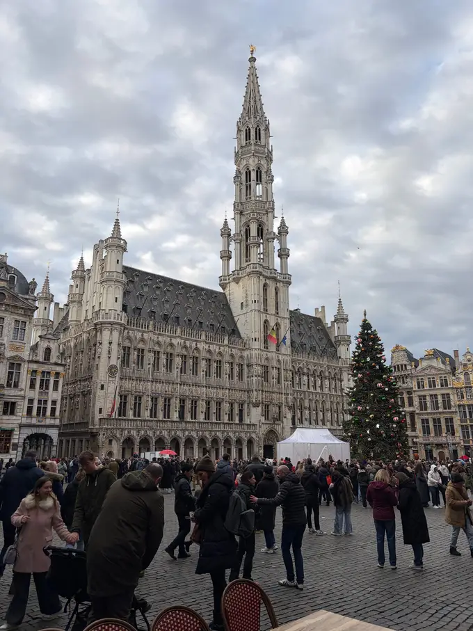 Das gotische Rathaus am Grand-Place bei bewölktem Himmel, rechts ein geschmückter Weihnachtsbaum, auf dem Platz viele Menschen