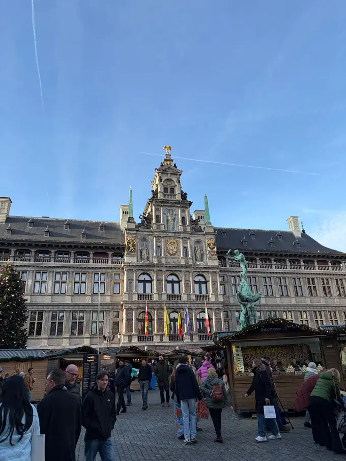 Das Rathaus am Grote Markt mit Fahnen, davor Holzbuden des Weihnachtsmarkts, der Brabobrunnen und ein Weihnachtsbaum, auf dem Platz viele Menschen